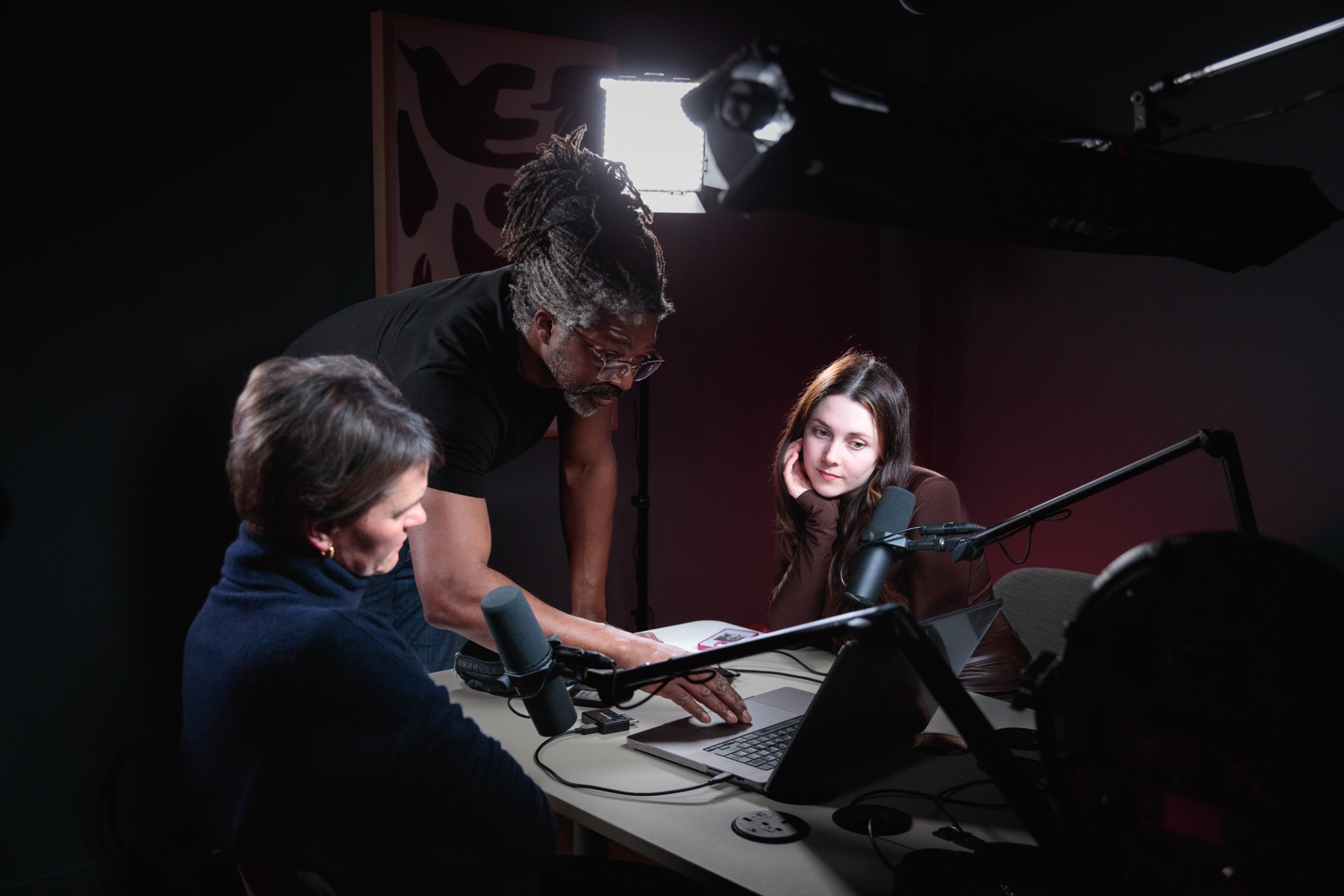 Kevan directing two speakers at a podcast desk under studio lights