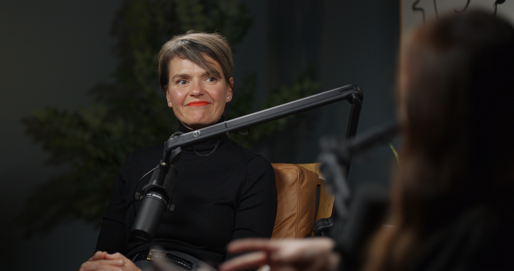 Finished podcast frame: host at the microphone on a warm, dark set